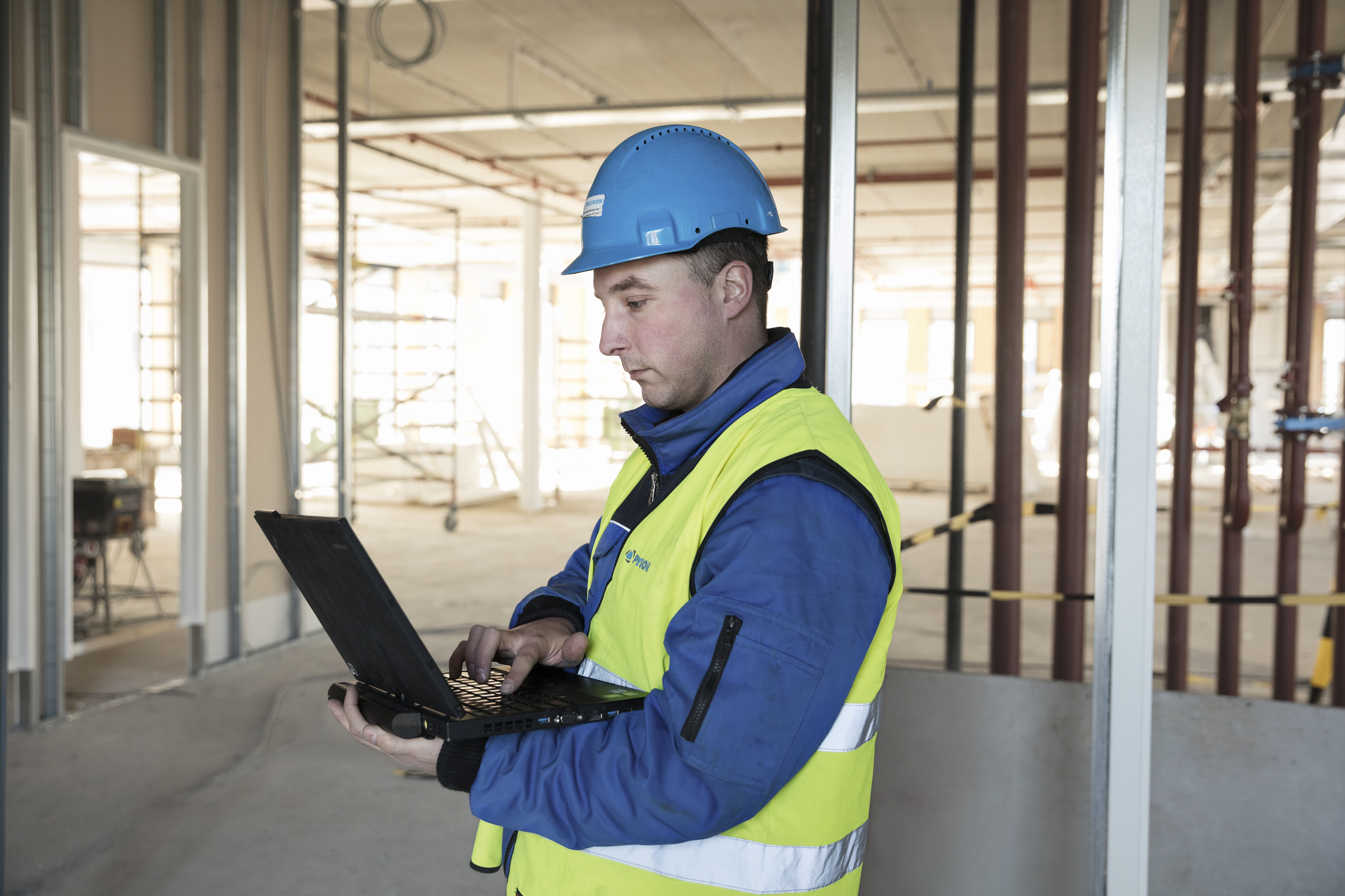 En byggnadsarbetare på en byggarbetsplats som håller i en bärbar dator. 